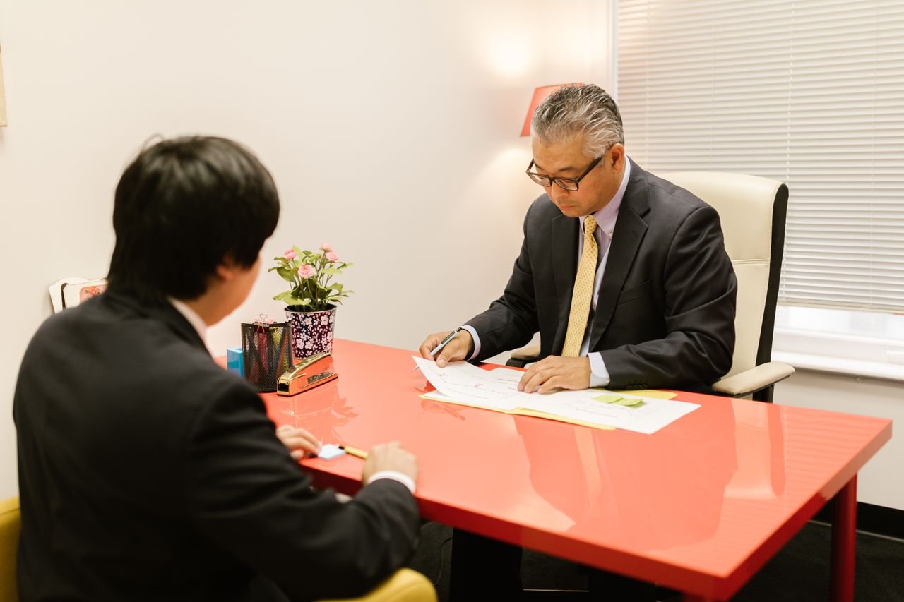Two professionals discussing documents in a modern office with a red desk.